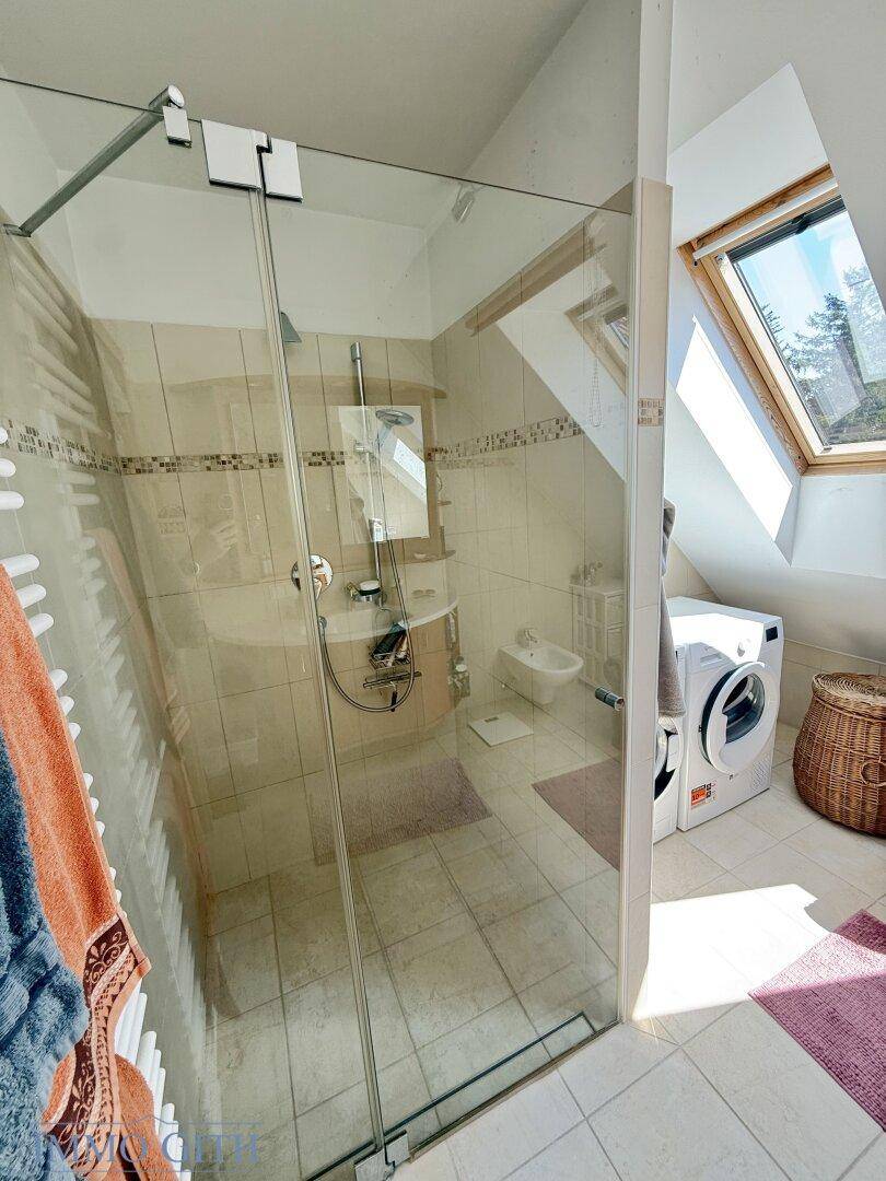 Geräumige Duschkabine mit Glasabtrennung in einem hellen Badezimmer mit Dachfenster.