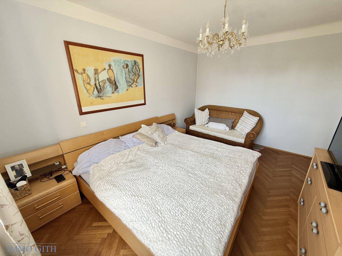 Gemütliches Schlafzimmer mit Doppelbett, Holzmöbeln, Parkettboden und einem Kronleuchter.