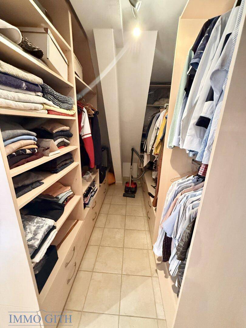 Praktischer begehbarer Kleiderschrank mit viel Stauraum und Fliesenboden unter einer Dachschräge.