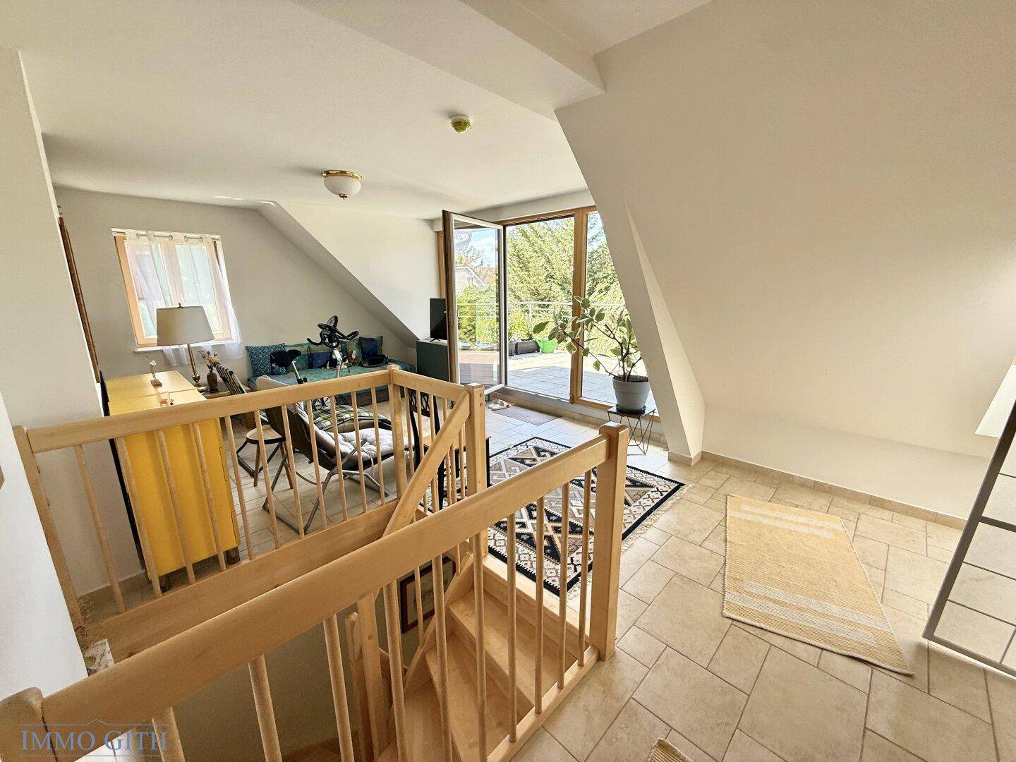 Heller Dachgeschoss-Wohnbereich mit Holztreppe und Zugang zu einem Außenbereich, unter Dachschrägen.