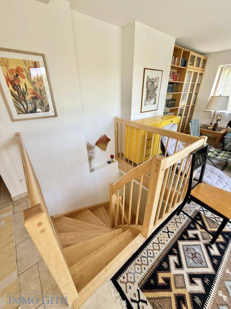 Gemütlicher Dachgeschossbereich mit Holztreppe, Bücherregal und dekorativen Bildern an den Wänden.