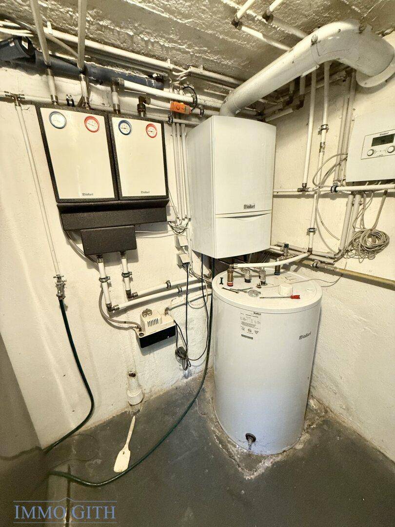 Heizungsanlage und Warmwasserboiler mit zahlreichen Rohrleitungen im Kellerraum installiert.