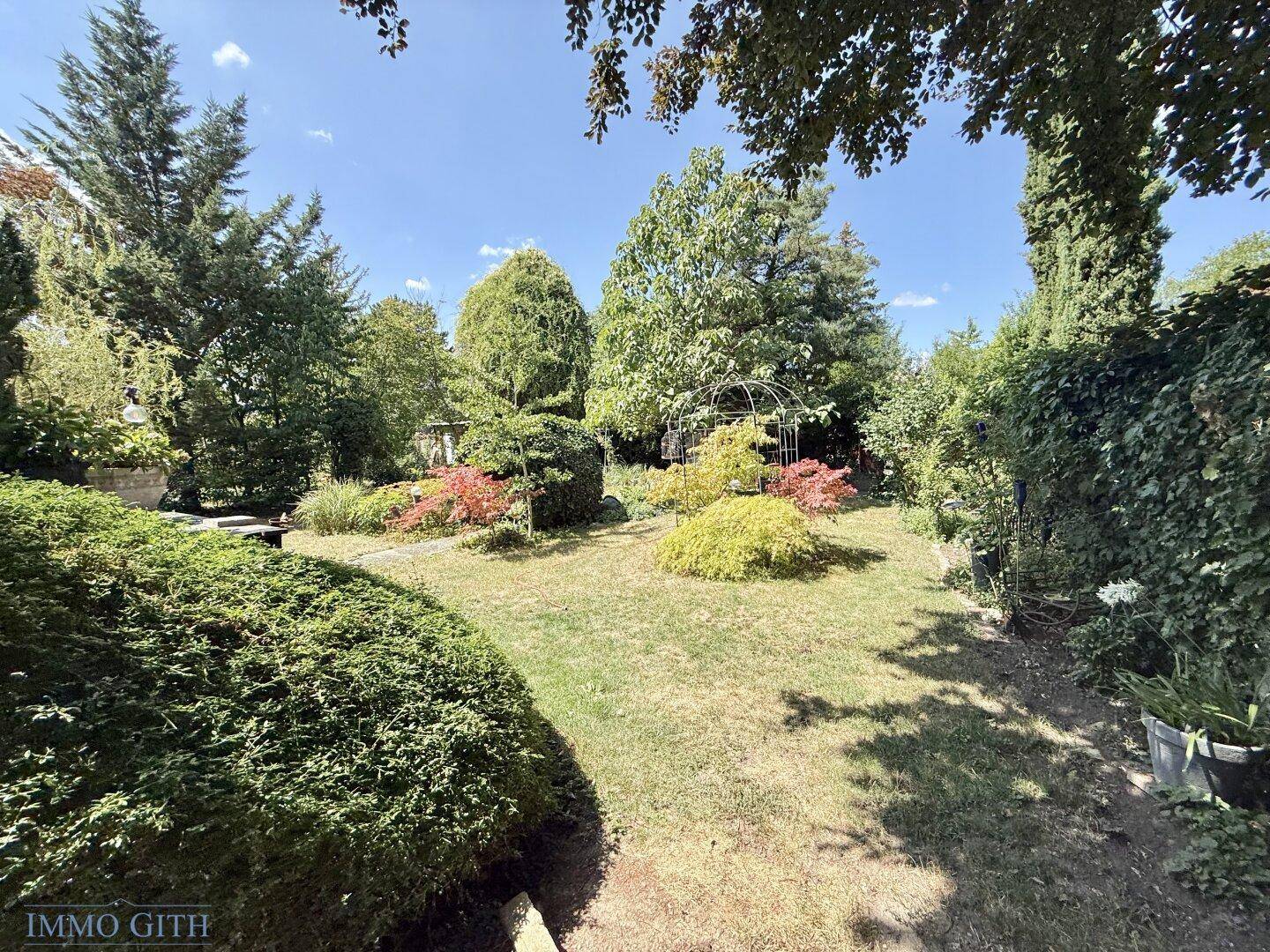 Weitläufiger, gepflegter Garten mit Rasenfläche, vielfältigen Pflanzen und Sträuchern an einem sonnigen Tag.