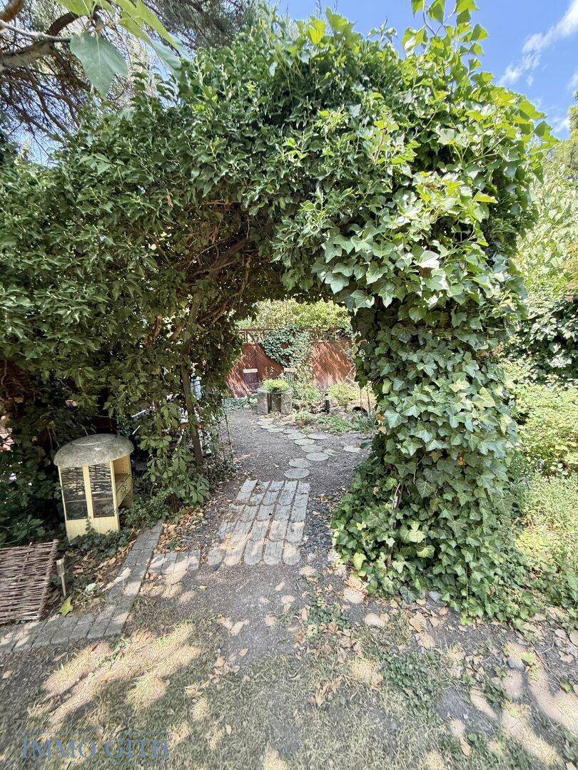 Idyllischer Gartenweg mit Trittsteinen, der durch einen von Efeu bewachsenen Torbogen führt.