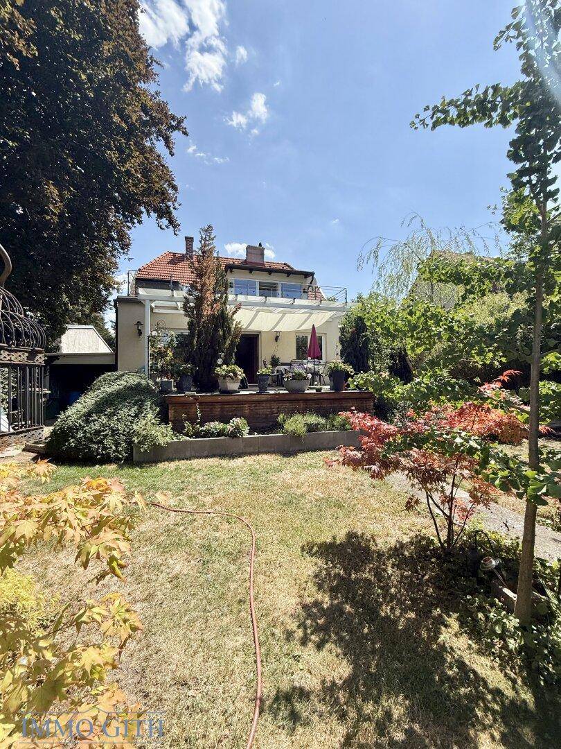 Rückansicht des Hauses vom Garten aus, mit einer Terrasse und einem Balkon im Obergeschoss.
