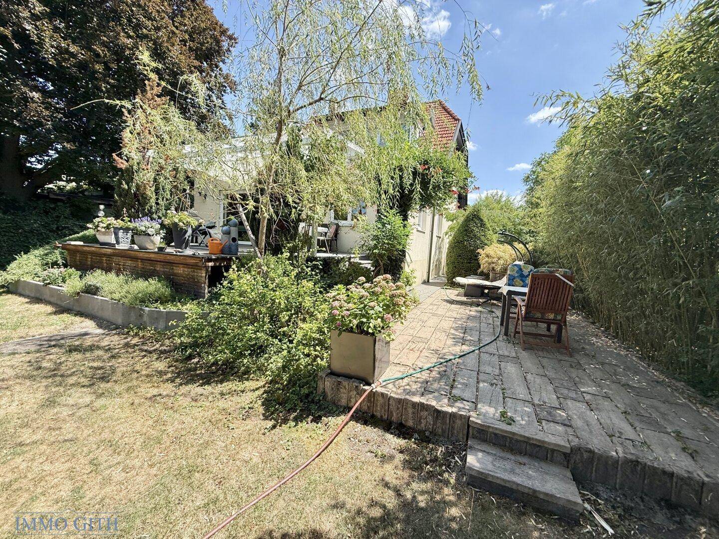 Gemütliche gepflasterte Terrasse mit Sitzgelegenheiten und Zugang zu einer erhöhten Holzterrasse am Haus.