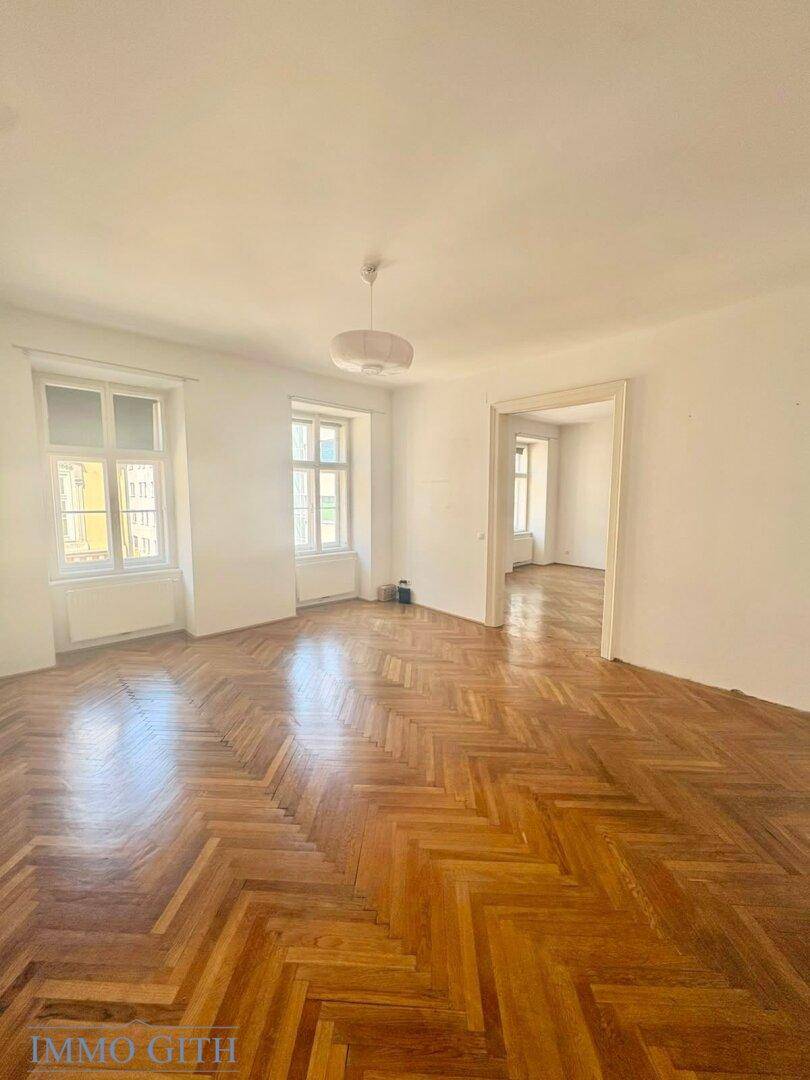 Helles Wohnzimmer mit Fischgrätparkett und Blick auf die Straße.