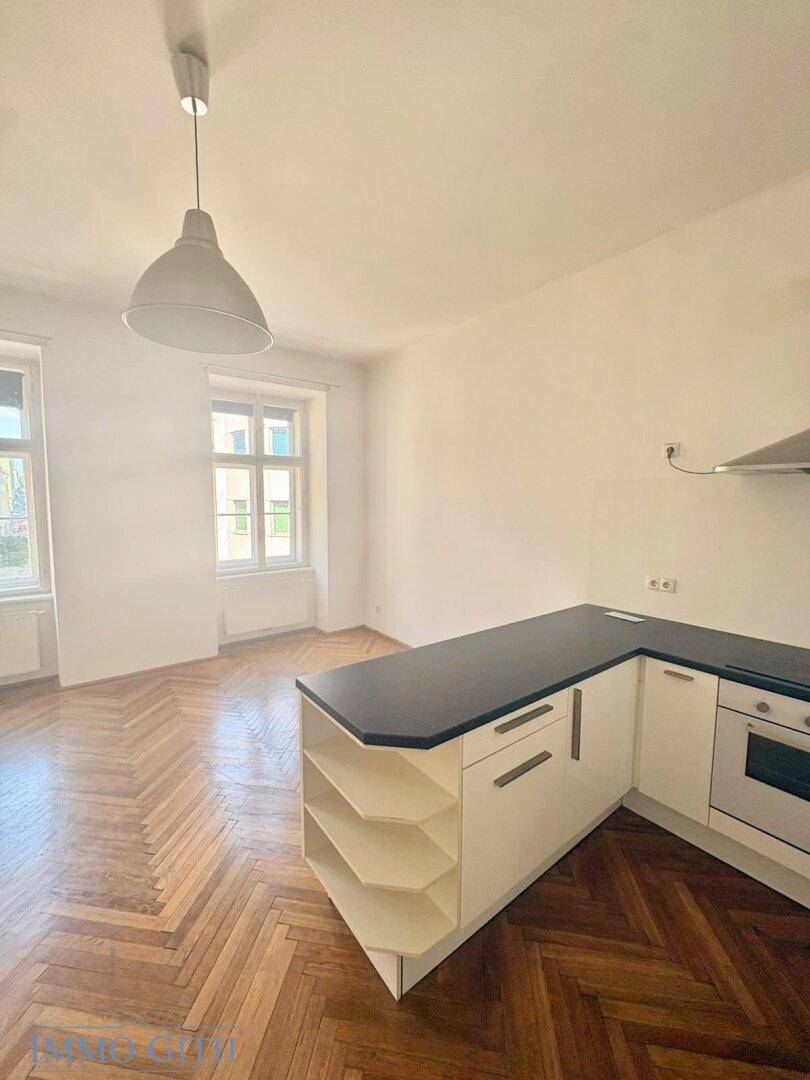 Moderne Küchenzeile mit weißen Schränken, dunkler Arbeitsplatte und integriertem Backofen.