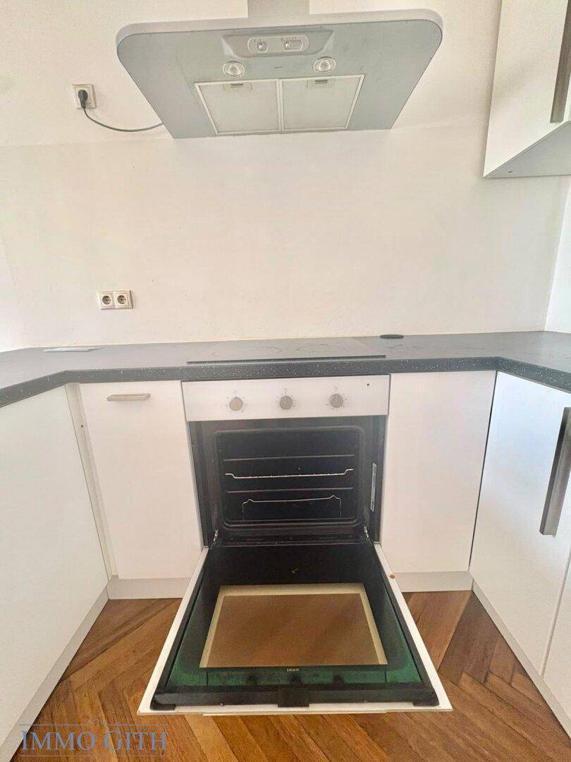 Moderner Einbaubackofen mit Dunstabzugshaube in einer weißen Küche.