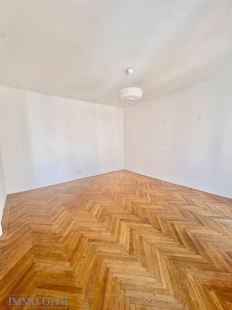 Helles Zimmer mit Fischgrätparkett und weiß gestrichenen Wänden.