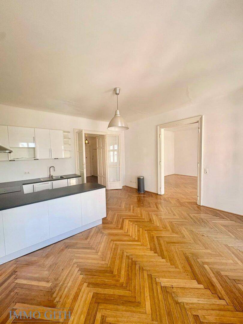Offener Wohnbereich mit moderner Küchenzeile, Fischgrätparkett und hohen Decken.