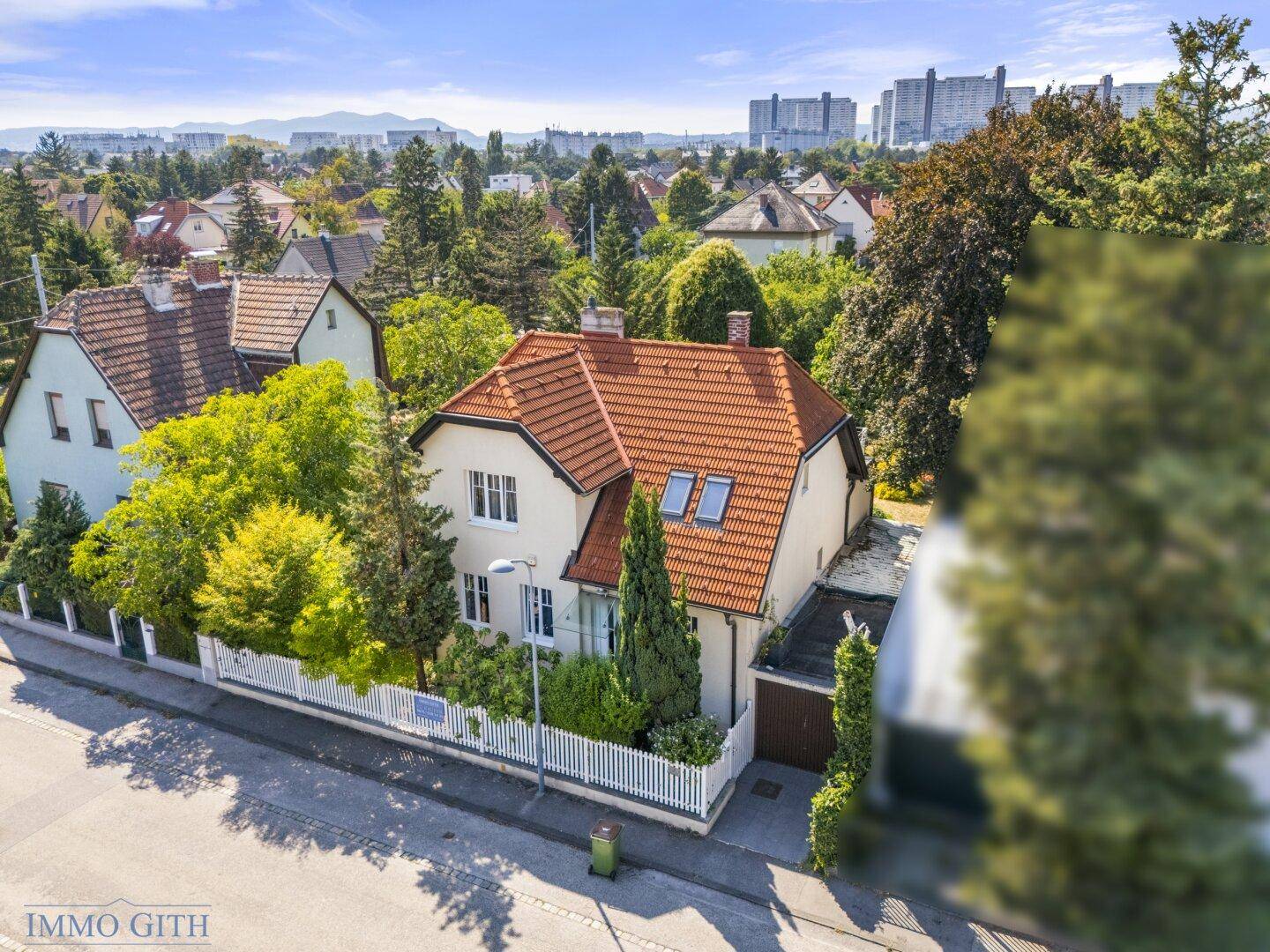 Luftaufnahme eines charmanten Hauses mit rotem Ziegeldach, umgeben von viel Grün und einem weißen Zaun.