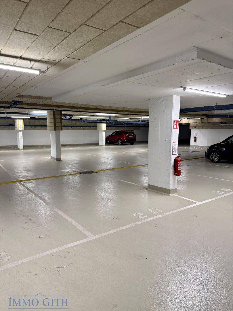 Geräumige Tiefgarage mit markierten Parkplätzen, Säulen und einem Feuerlöscher an der Wand.