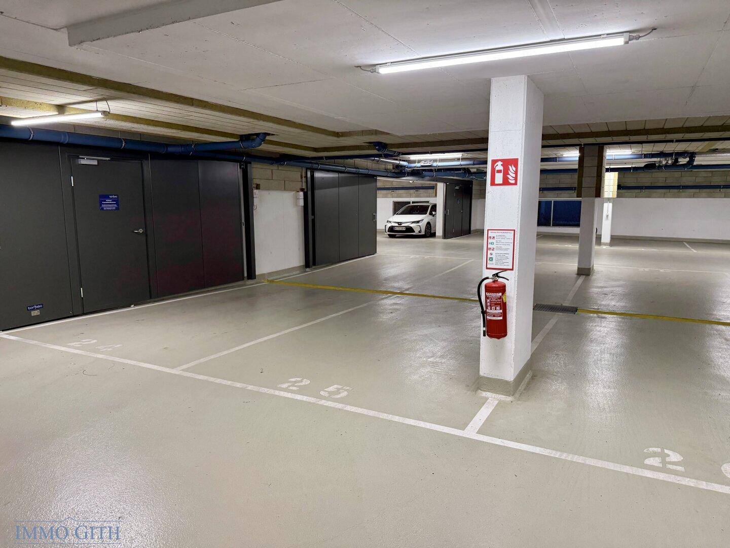 Saubere Tiefgarage mit markierten Stellplätzen und privaten Lagerabteilen an der Seite.