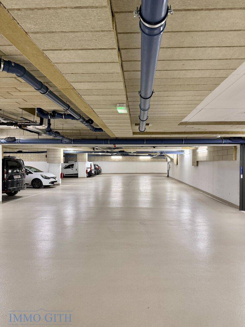 Lange, gut beleuchtete Tiefgarage mit sichtbaren blauen Versorgungsleitungen an der Decke.