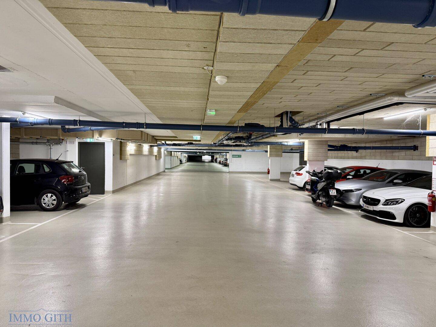 Weitläufige Tiefgarage mit vielen Parkplätzen und Fahrzeugen auf beiden Seiten des Ganges.