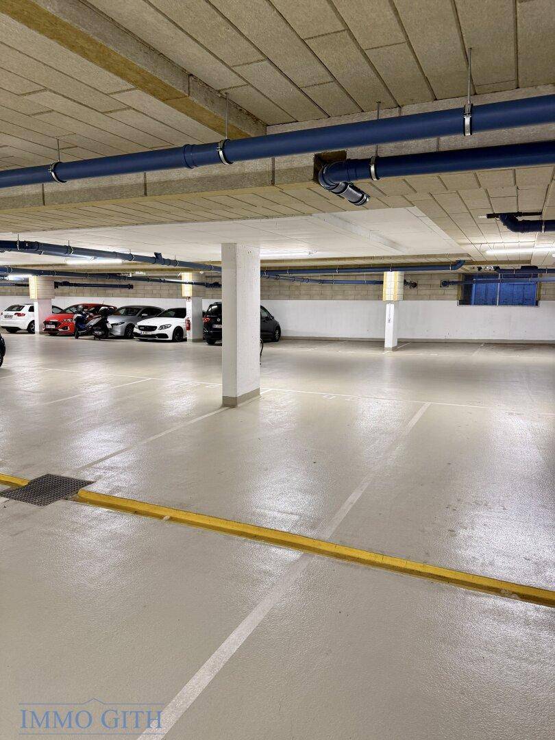 Tiefgarage mit gelber Fahrbahnmarkierung und sichtbaren blauen Versorgungsrohren an der Decke.