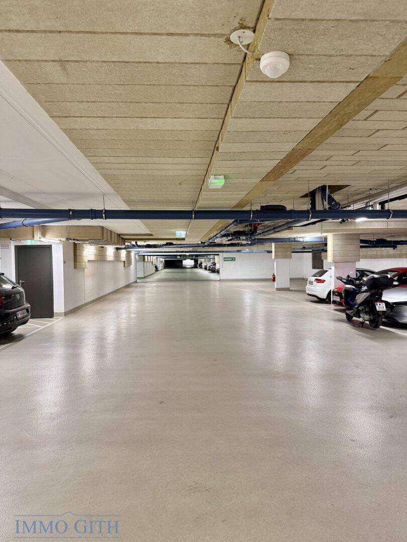 Heller Gang in der Tiefgarage mit parkenden Autos und effizienter Deckenbeleuchtung.