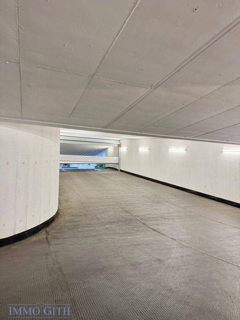 Ausfahrt einer Tiefgarage mit geschwungenen Betonwänden und strukturierter Fahrbahn nach oben.