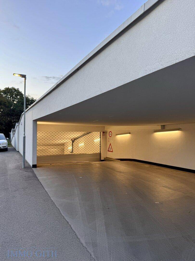 Eingangsbereich einer modernen Tiefgarage mit Rolltor und angrenzender Straße bei Dämmerung.