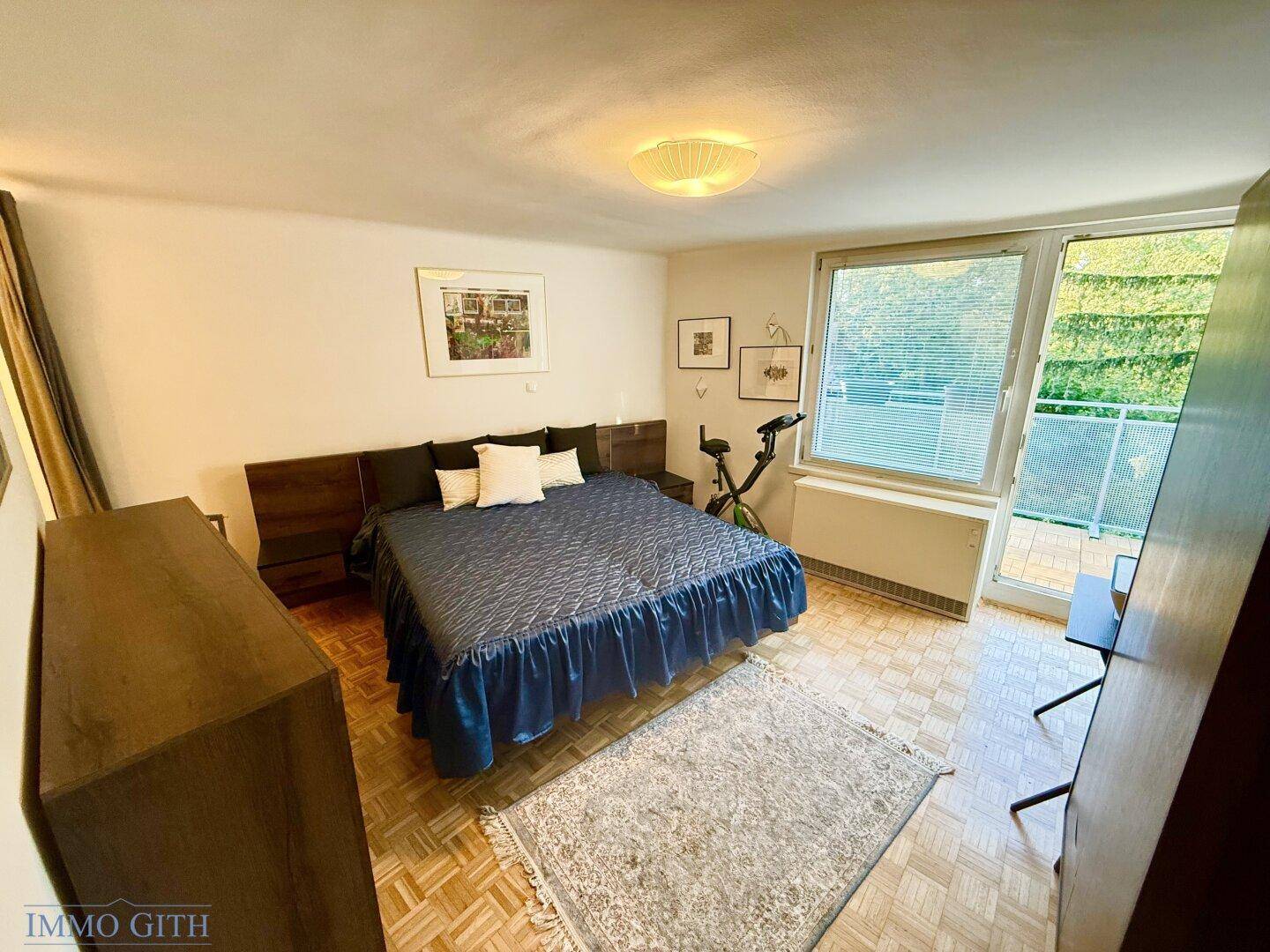 Helles Schlafzimmer mit Doppelbett, Parkettboden und direktem Zugang zum Balkon.
