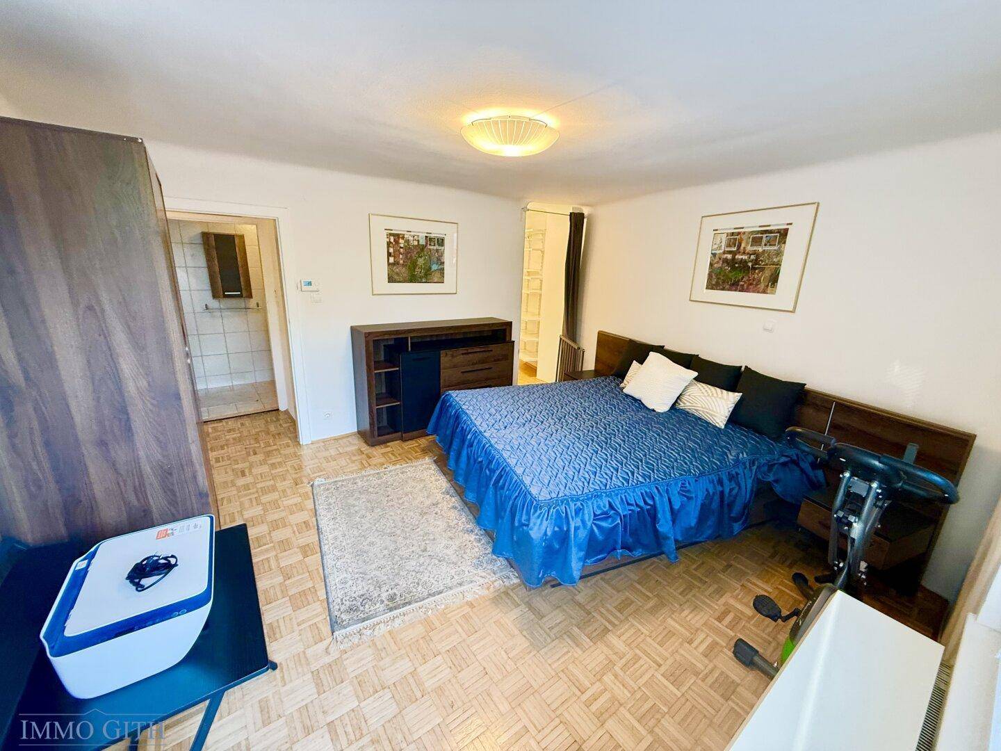 Gemütliches Schlafzimmer mit Parkettboden und Zugang zu einem weiteren Raum.