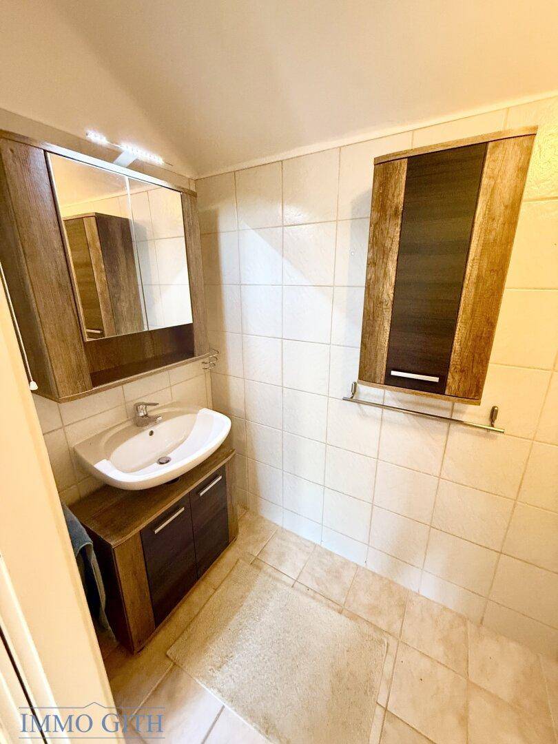 Badezimmer mit Waschbecken, Spiegelschrank und Fliesenboden in neutralen Farben.