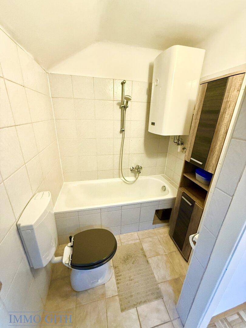 Badezimmer mit Badewanne, Toilette und Fliesenboden, ausgestattet mit einem Warmwasserboiler.