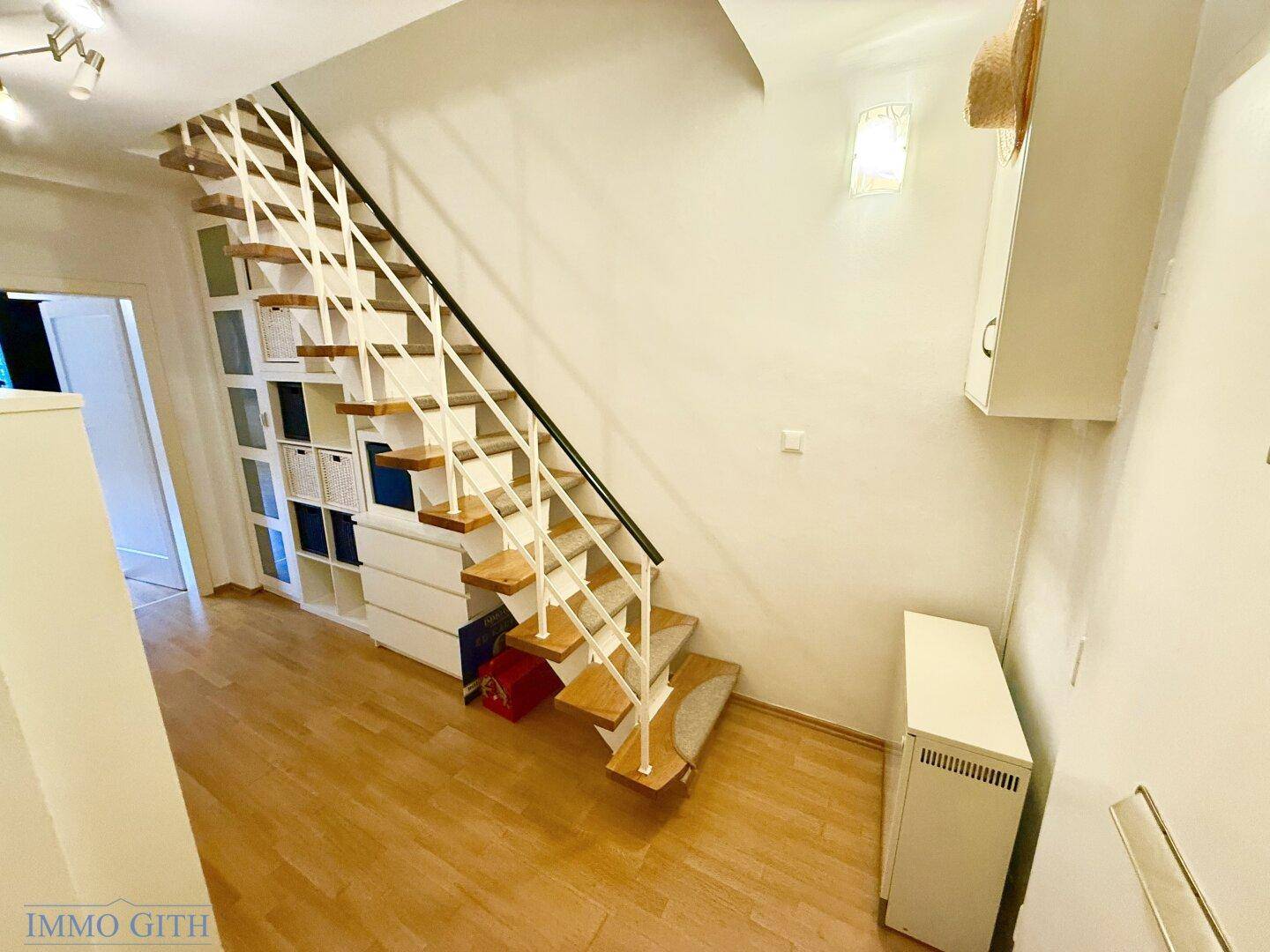 Heller Flur mit Holztreppe und integriertem Stauraum, verbindet die verschiedenen Ebenen.