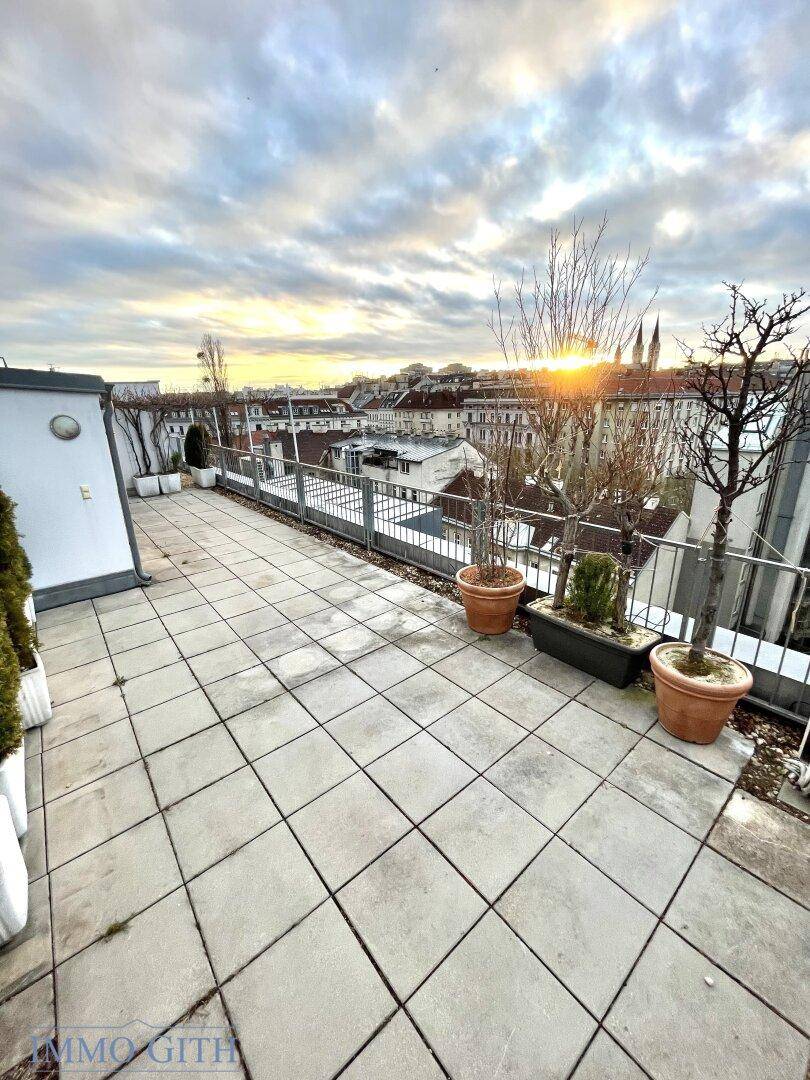 Weitläufige Dachterrasse mit Fliesenboden und Panoramablick über die Stadt bei Sonnenuntergang.
