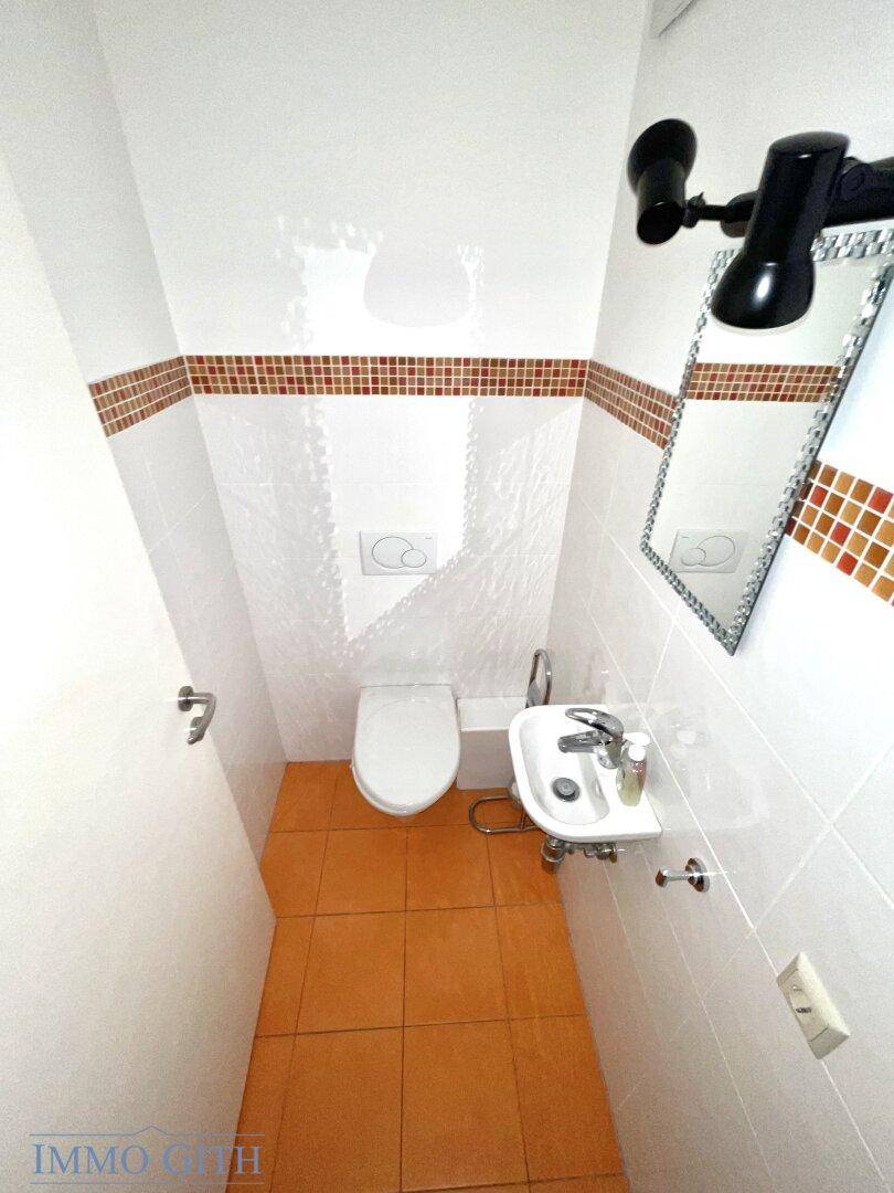 Kleines Gäste-WC mit Terrakotta-Fliesen, Wand-WC und einem kleinen Waschbecken.