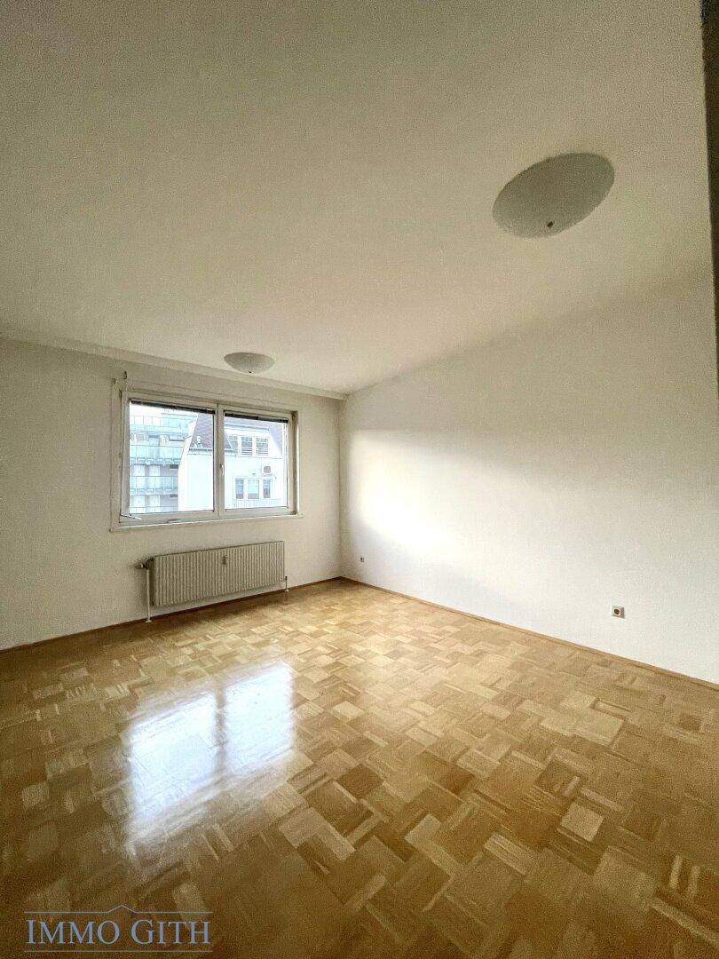 Helles Schlafzimmer mit Parkettboden und Fenster, bereit zur individuellen Gestaltung.