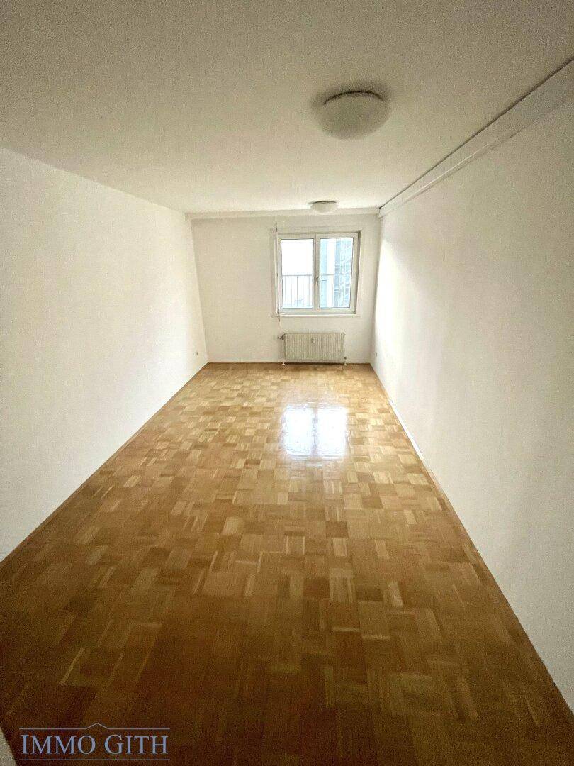 Langes Schlafzimmer mit Parkettboden und einem Fenster, das viel Licht hereinlässt.