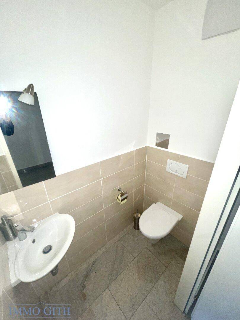 Modernes Gäste-WC mit beigen Fliesen, Wand-WC und kleinem Waschbecken.