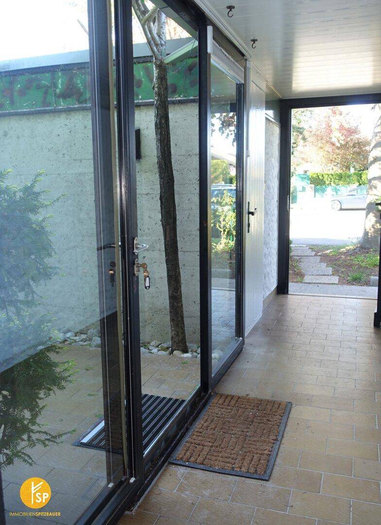 Heller Eingangsbereich mit großen Glasfronten, Fliesenboden und Blick auf den Außenbereich.