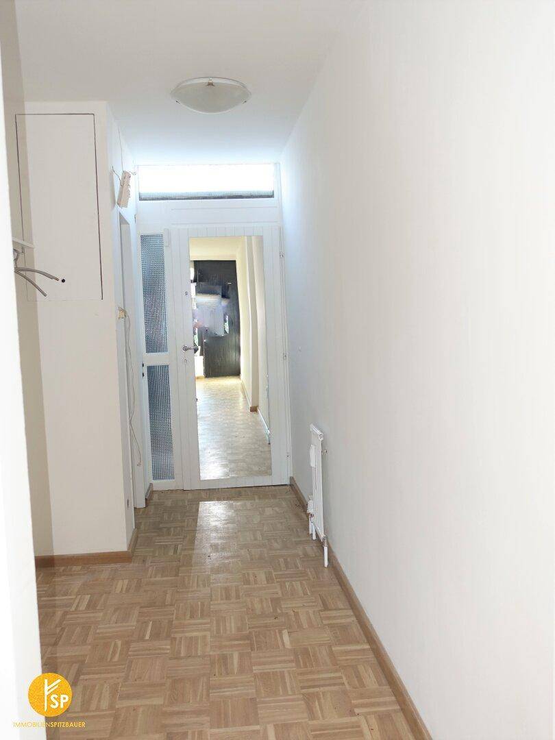 Langer, heller Flur mit Holzparkettboden und Garderobe, der zum Eingangsbereich führt.