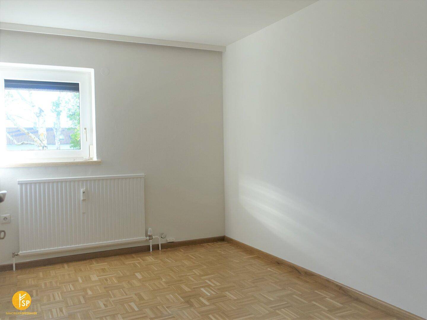 Helles Schlafzimmer mit Fenster, Heizkörper und klassischem Holzparkettboden.