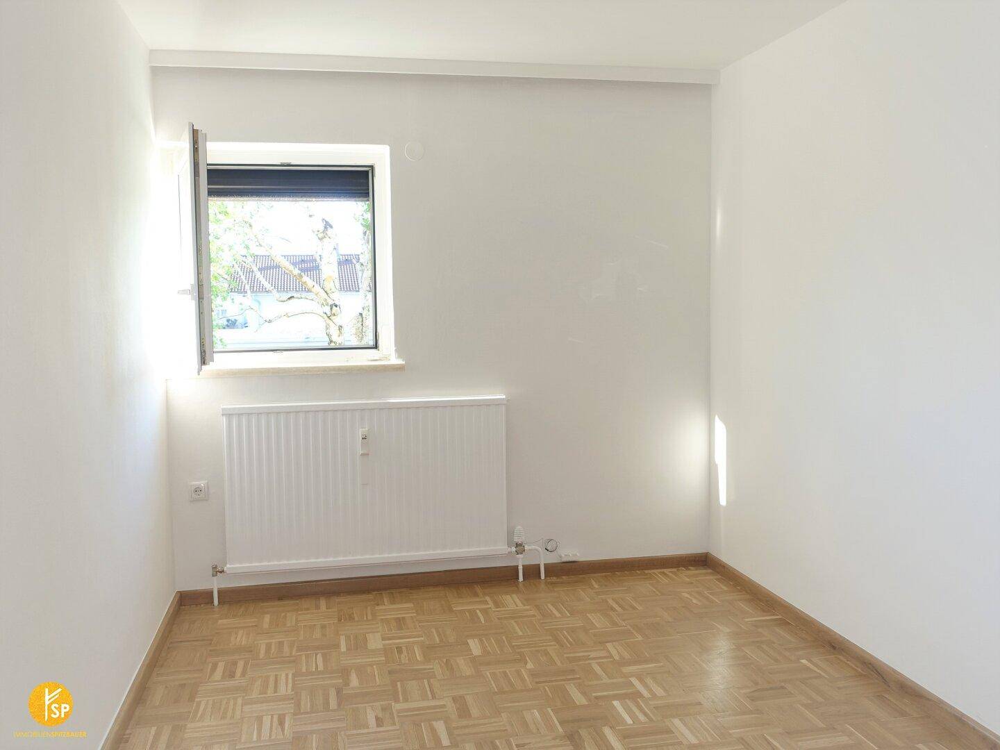 Freundliches Zimmer mit Parkettboden, Heizkörper und Fenster für natürliches Licht.