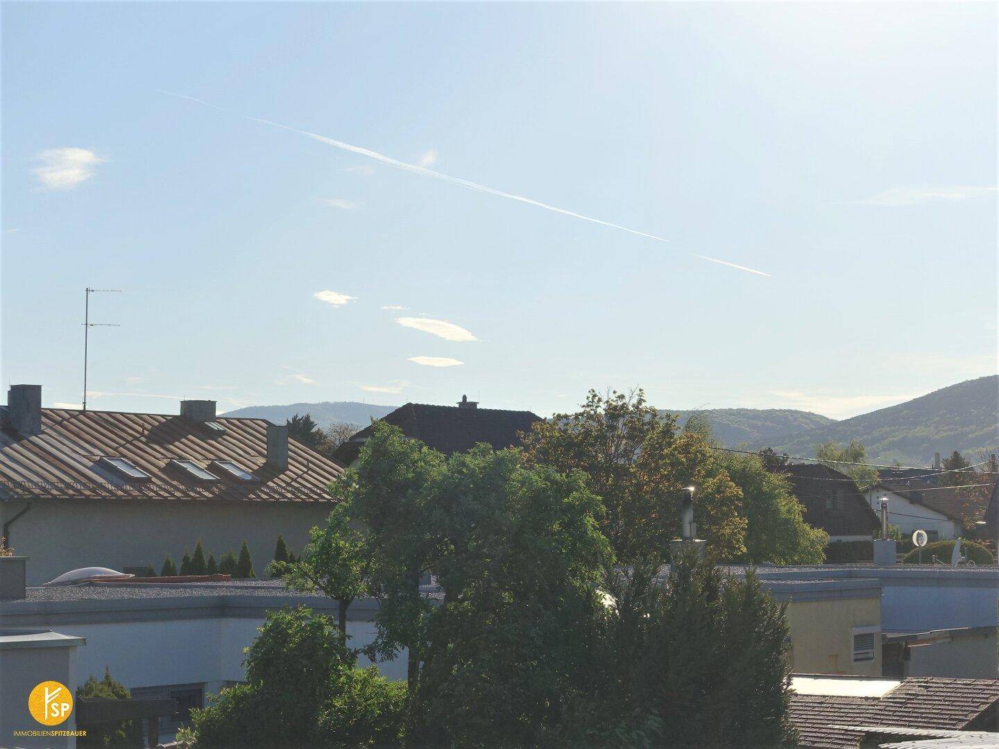 Weitläufiger Blick über Dächer und grüne Hügel unter einem klaren blauen Himmel.