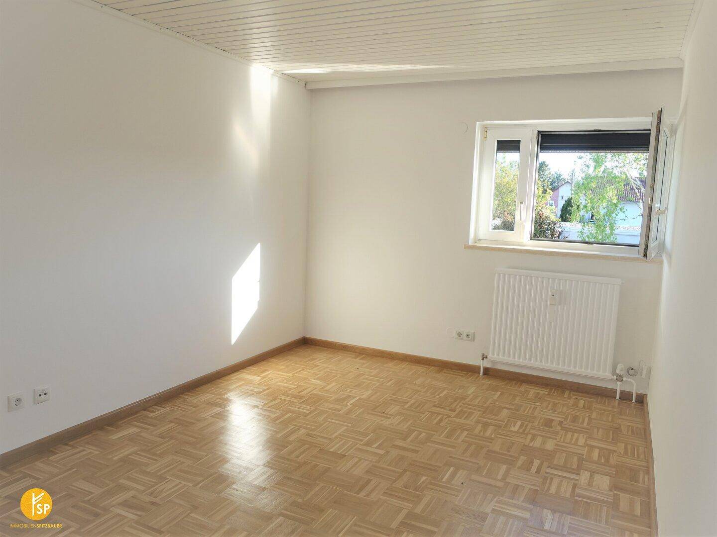 Helles Zimmer mit Parkettboden, weißen Wänden und Fenster mit viel Tageslicht.