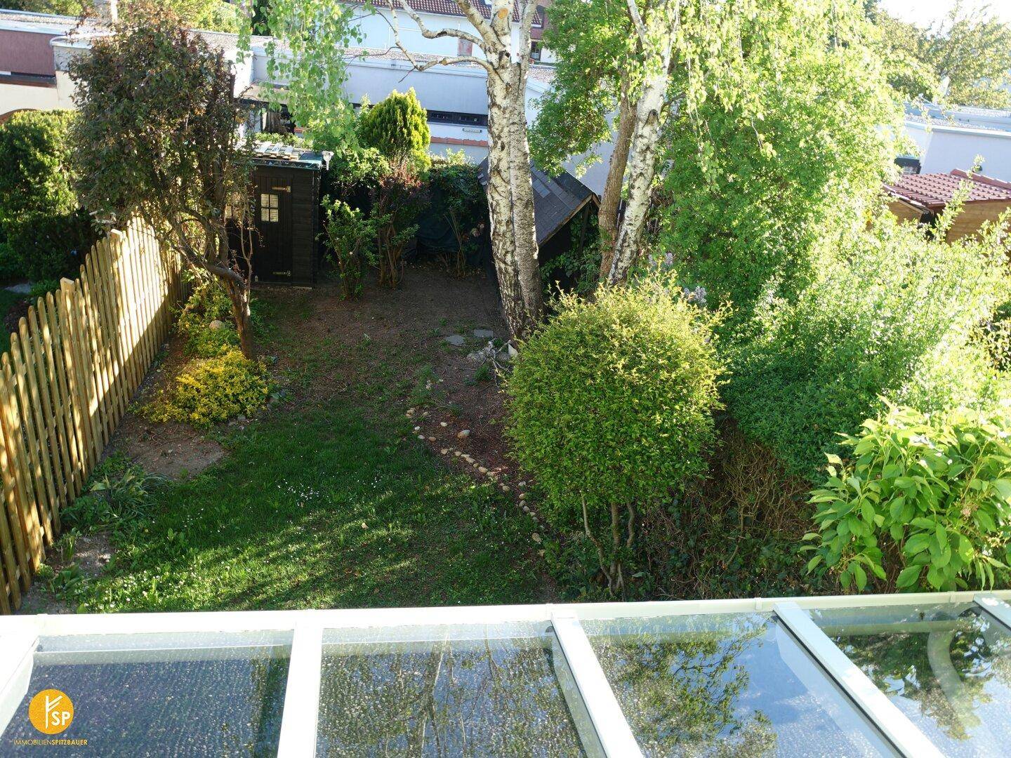 Vogelperspektive auf den Garten mit Rasen, Bäumen und einem kleinen Gartenhaus.