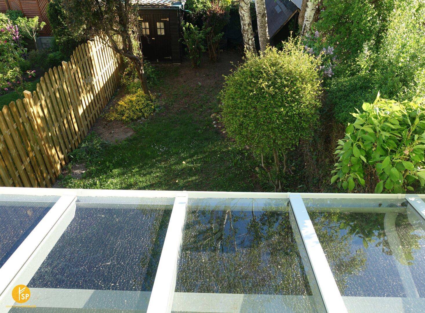 Sonniger Blick von oben auf den Garten mit Rasen, Bäumen und Gartenhaus.
