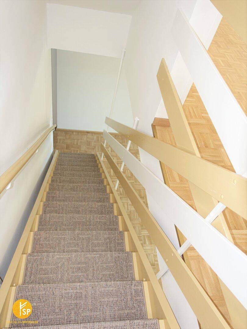 Treppenhaus mit Teppichboden und Holzgeländer, das die verschiedenen Etagen verbindet.