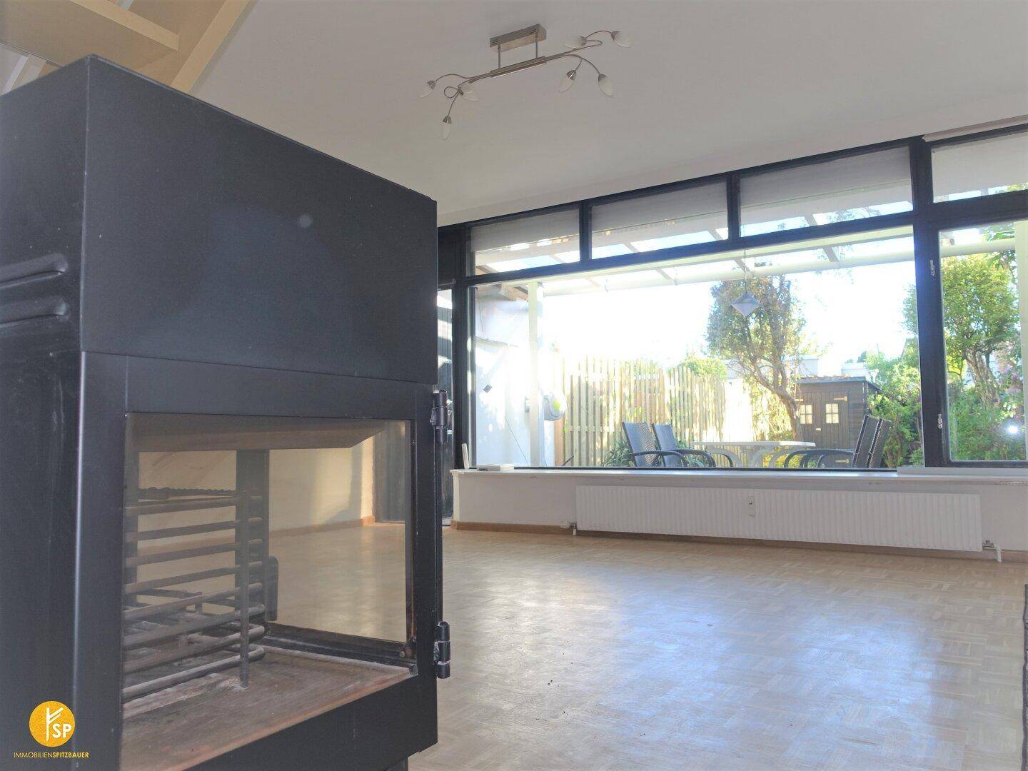 Helles Wohnzimmer mit großem Fenster, Blick in den Garten und modernem Kaminofen.