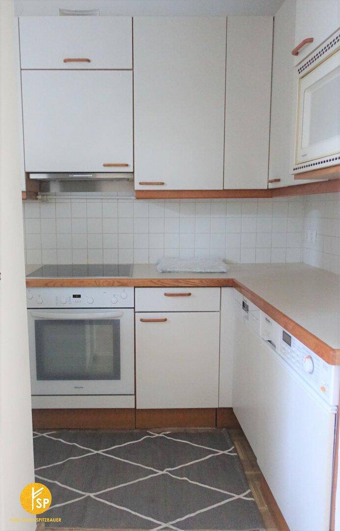 Funktionale Küche mit weißen Schränken, Holzarbeitsplatten und integrierten Geräten.