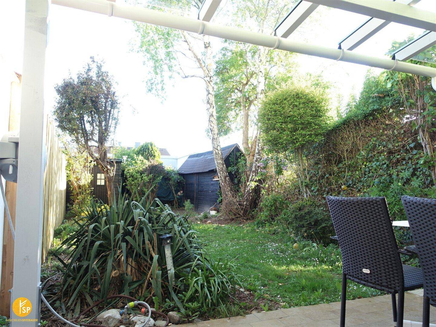 Blick von der Terrasse in den grünen Garten mit Rasenfläche und üppiger Bepflanzung.
