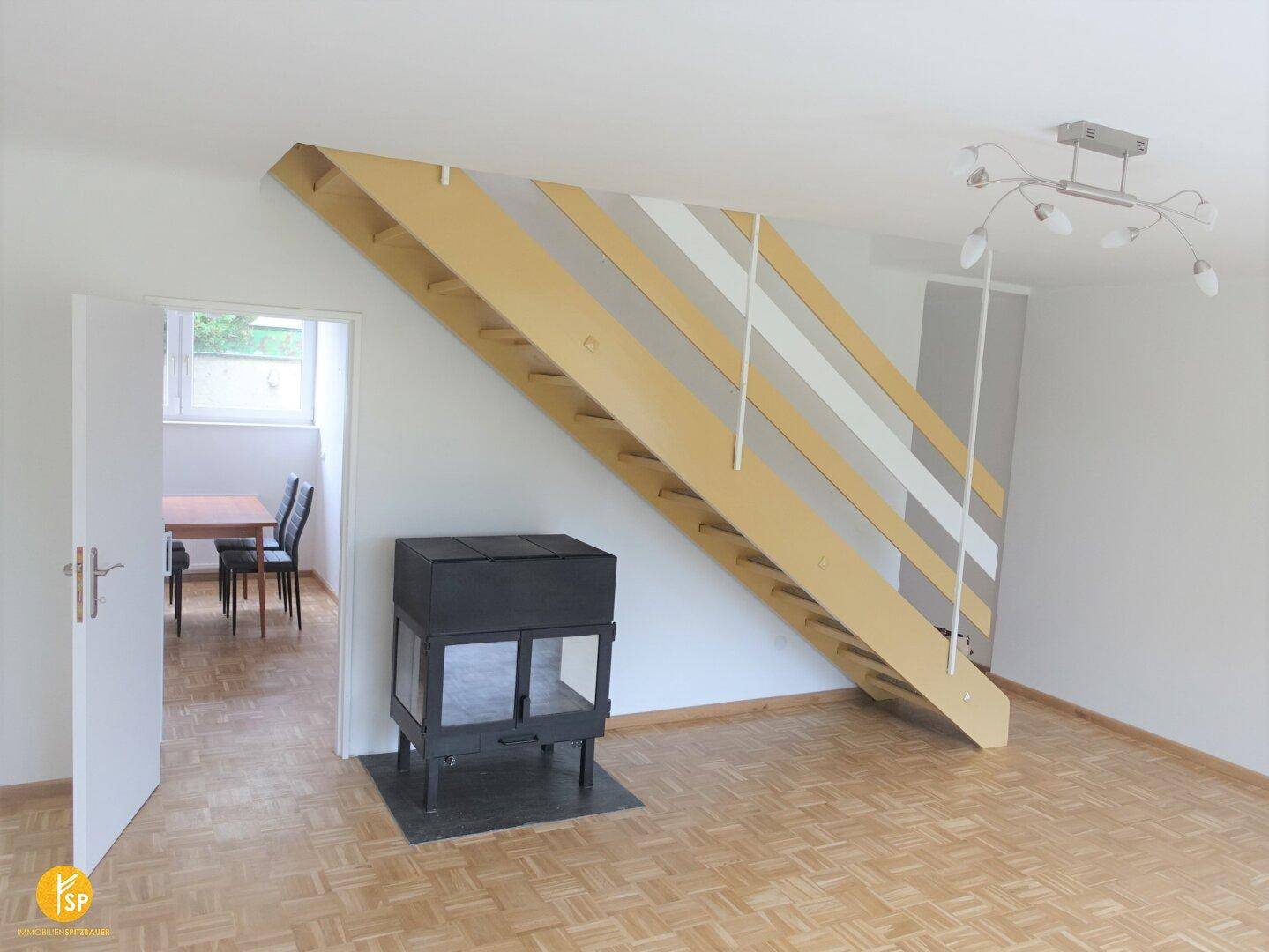 Geräumiges Wohnzimmer mit Kamin, Holzparkettboden und offener Treppe zum oberen Bereich.