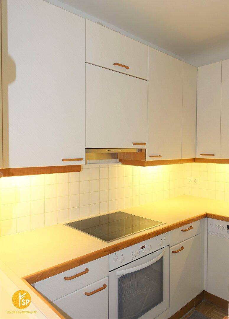 Funktionale Küche mit weißen Schränken, Holzarbeitsplatte und integriertem Kochfeld und Backofen.