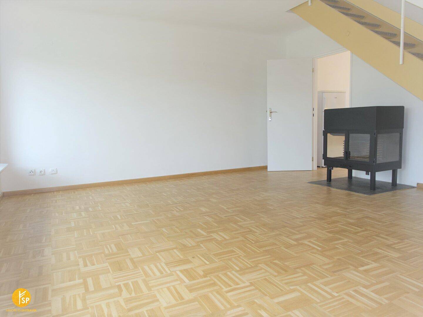Heller Wohnbereich mit Holzparkettboden, modernem Kamin und offener Treppenkonstruktion.