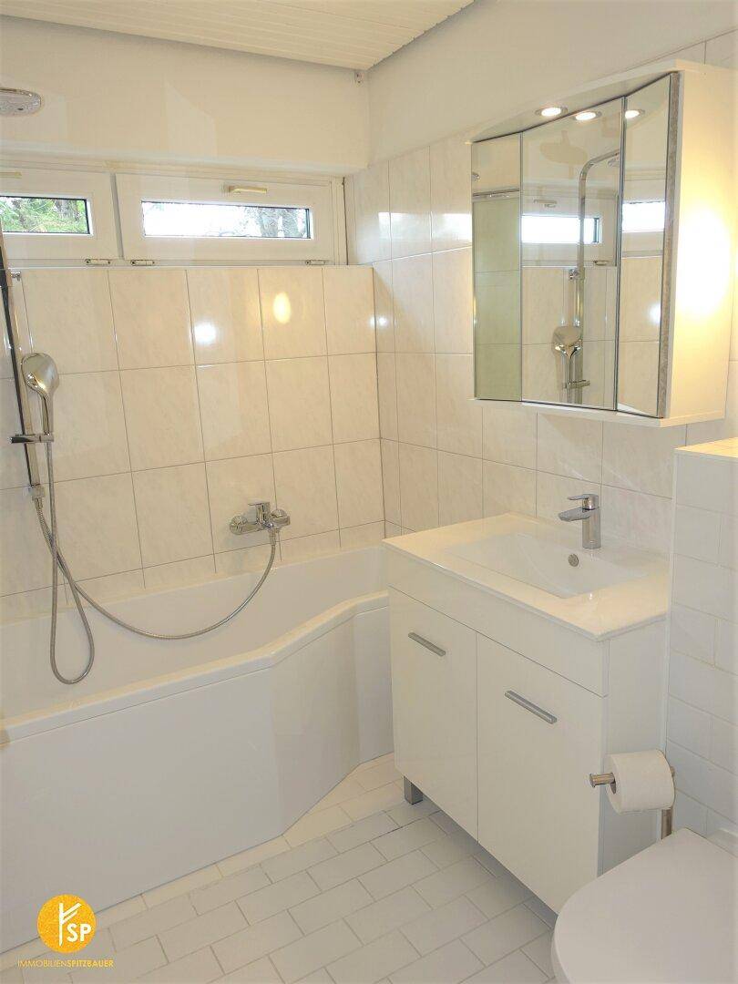 Modernes Badezimmer mit weißen Fliesen, Badewanne mit Duschfunktion und Fenster.